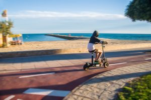 Guy riding electric scooter along autumn beach.