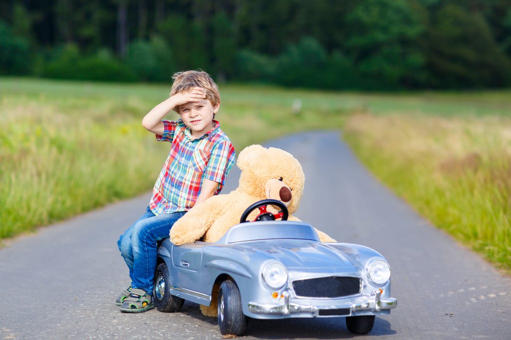 Little kid boy driving big toy car with a bear, outdoors.
